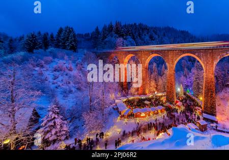 Mercatino di Natale nella Gola di Ravenna nella Foresta Nera innevata, il viadotto ferroviario della Hoellentalbahn è illuminato con colori vivaci, Foresta Nera Foto Stock