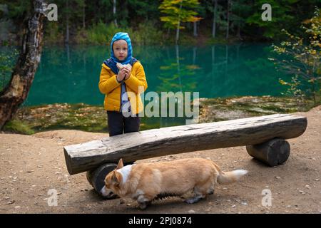 Un bambino e un cane riposano su una panchina vicino ad un bellissimo lago turchese. Montagne polacche Foto Stock