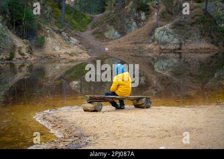 Il bambino sta riposando su una panchina al bordo del lago nel mezzo della foresta. Montagne polacche Foto Stock