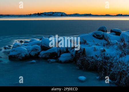 Uno splendido tramonto invernale illumina il tranquillo mare ghiacciato e la terra innevata della Svezia, mostrando la bellezza della natura. Foto Stock