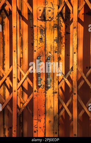 Un primo piano verticale di due vecchie porte arancioni con maniglie in stile antico Foto Stock