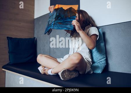 Curiosa studentessa impegnata nel libro che passa il tempo nella biblioteca scolastica. L'allievo della scuola elementare è interessato alla lettura del libro. Bambino che fa i compiti. GI intelligente Foto Stock