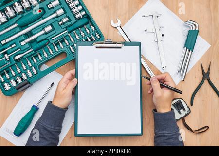 Uomo che lavora in officina tenendo gli appunti utilizzando molti strumenti. Chiave, chiave, pinza e cricchetto con molti accessori. Attrezzature. Utensile universale se Foto Stock