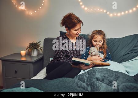 Mamma che legge libro sua figlia a letto prima di andare a dormire. Leggere storie prima di dormire. Storie di sonno per i bambini Foto Stock