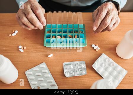 Uomo anziano che organizza il suo farmaco in un dispenser di pillole. Uomo anziano che prende le pillole dalla scatola. Assistenza sanitaria e concetto di vecchiaia con farmaci. Medicamenti Foto Stock