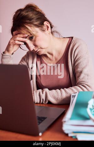 La donna si è concentrata sul suo lavoro lavorando sodo facendo il suo lavoro in remoto su un notebook da casa. Donna seduta alla scrivania di fronte al computer che guarda lo schermo Foto Stock