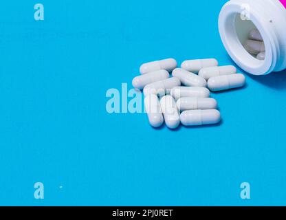 Pillole versate fuori dalla bottiglia bianca su sfondo blu. Mock up per le offerte speciali come la pubblicità o altre idee. Medico, farmacia e assistenza sanitaria conce Foto Stock