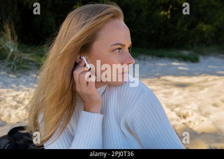 Felice giovane donna sulla spiaggia mare oceano. Indossando cuffie wireless che fanno audio healing Sound Therapy essere memdful tempo libero in natura. Benessere unità con la natura salute consapevolezza. Godetevi il relax all'aperto Foto Stock