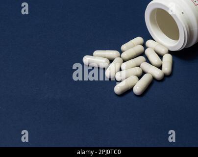 Pillole versate fuori dalla bottiglia bianca su sfondo blu. Mock up per le offerte speciali come la pubblicità o altre idee. Medico, farmacia e assistenza sanitaria conce Foto Stock