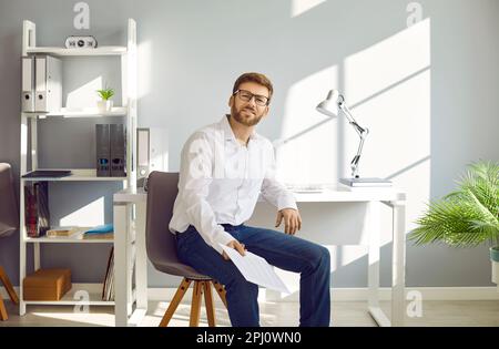 Ritratto di un giovane uomo d'affari seduto sulla sedia sul suo posto di lavoro Foto Stock