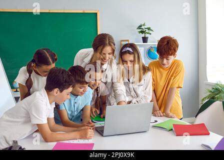 Bambini intelligenti ragazzi e ragazze alunni si trovano di fronte al computer portatile con un'insegnante femminile nella scuola elementare Foto Stock