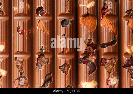 Sfondo cioccolato. Cioccolato al latte con mandorle, uva passa, bacche secche primo piano come sfondo. Foto Stock