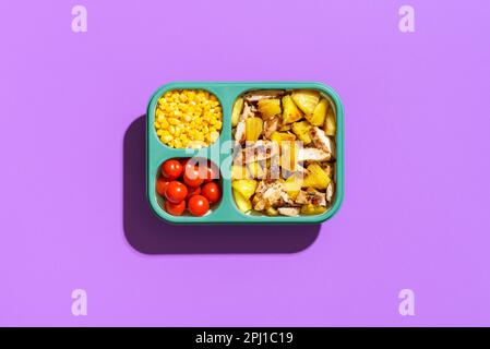 Vista dall'alto con pollo hawaiano e insalata di ananas in un pranzo al sacco, minimalista su un tavolo viola. Piatto dolce e asino, ananas arrosto e pollo me Foto Stock