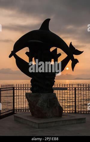 Preso come il sole sta scendendo dietro la statua dei due Delfini a Rethymnon, Creta, Grecia. Foto Stock