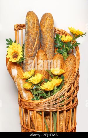 Baguette fresche con semi di sesamo, semi di papavero e semi di girasole in un cesto intrecciato con fiori di girasole decorativi. Immagine verticale. Foto Stock