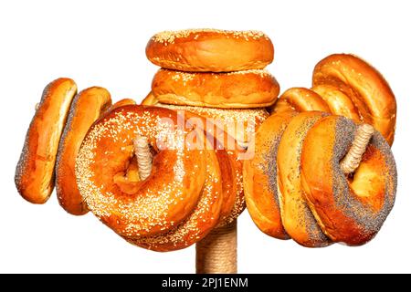 Gli appetitosi bagel sono sormontati con semi di sesamo e semi di papavero appesi su una rastrelliera. Isolato su sfondo bianco. Messa a fuoco selettiva. Foto Stock