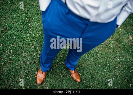Un giovane uomo elegante si erge in erba verde lussureggiante in un paio di pantaloni blu Foto Stock