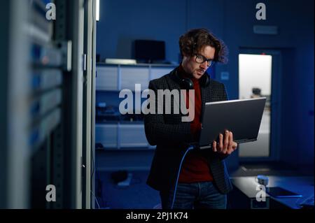 Ingegnere dei dati che tiene in mano un computer portatile mentre lavora con un supercomputer nella sala server Foto Stock