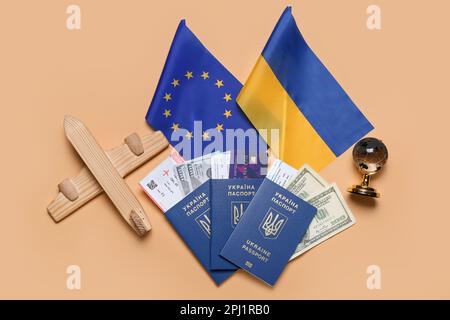 Passaporti con denaro, aeroplano giocattolo, bandiere dell'Ucraina e dell'Unione europea su sfondo beige Foto Stock