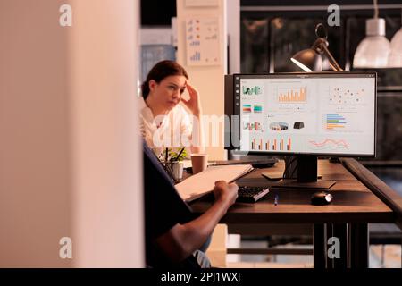 Gli impiegati che analizzano i dati di analisi di rapporto sul calcolatore, confrontano i grafici sugli appunti, analisi di risultati di ricerca dell'azienda. African american businessman che controlla le statistiche in ufficio Foto Stock