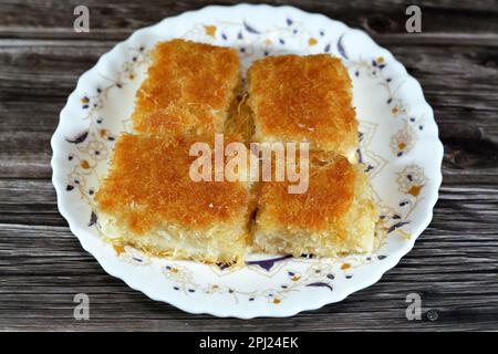 Un tradizionale dessert mediorientale Knafeh Konafa fatto con kataifi di pasta filata, imbevuto in uno sciroppo di miele di zucchero dolce, stratificato con formaggio, o coagulato Foto Stock