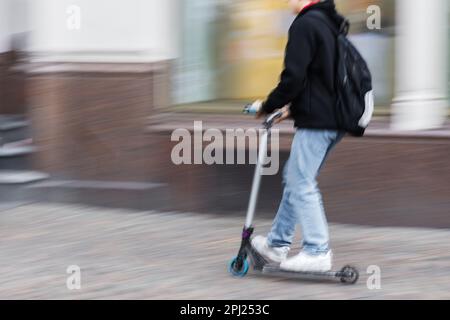 immagine con fotocamera fatto effetto sfocatura movimento di un giovane non identificato con zaino su uno scooter calcio in città Foto Stock