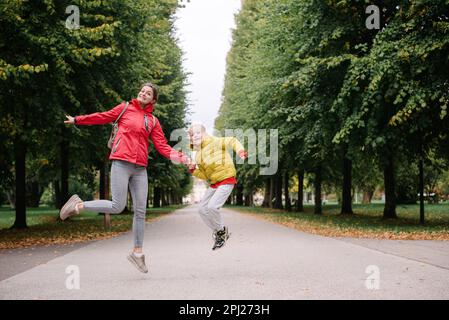 Madre e figlio saltano nel parco autunnale. Stagione autunnale. Felice giovane bella madre e suo figlio hanno una passeggiata nel parco Foto Stock