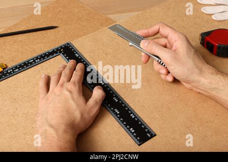 Uomo che taglia il bordo del truciolo con il coltello di utilità ed il righello, primo piano Foto Stock