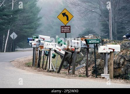 Il gruppo di caselle postali su strada si affollano su una strada rurale di campagna curvilinosa nella costa meridionale del Maine Foto Stock