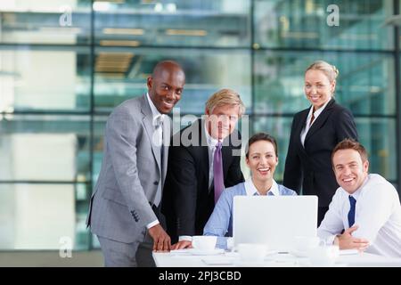 Team aziendale sicuro. Uomini d'affari multietnici di successo sorridenti con il laptop sul tavolo. Foto Stock