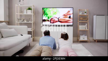 Giovane coppia felice giacente su un tappeto o guardare film in televisione a casa Foto Stock