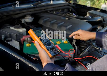 Tecnico che controlla la tensione della batteria del veicolo Foto Stock