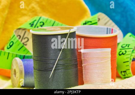 Utensili per cucire isolati su indumenti colorati con macro dettagli tra cui spole di filo, ago e metro a nastro. Foto Stock