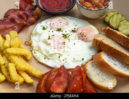 Colazione inglese sana con uova fritte, pancetta, patatine fritte, fagioli e pomodori primo piano Foto Stock