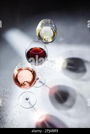 Rosa rosa, rosso e bianco bicchieri da vino su sfondo chiaro con ombre. Vista dall'alto. Foto Stock