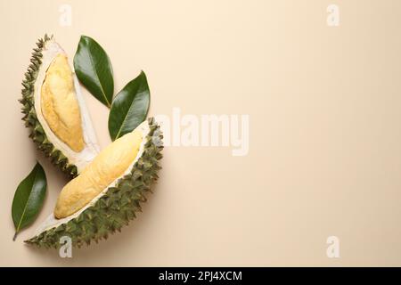 Pezzi di durian fresco maturo e foglie su sfondo beige, giacitura piatta. Spazio per il testo Foto Stock