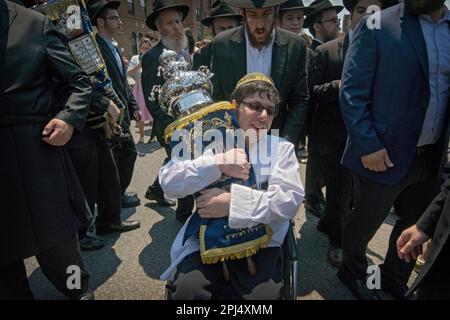 In occasione della celebrazione della scrittura di una nuova Torah, un giovane ebreo su sedia a rotelle abbraccia con passione il rotolo. A far Rockaway, Queens, New York City. Foto Stock
