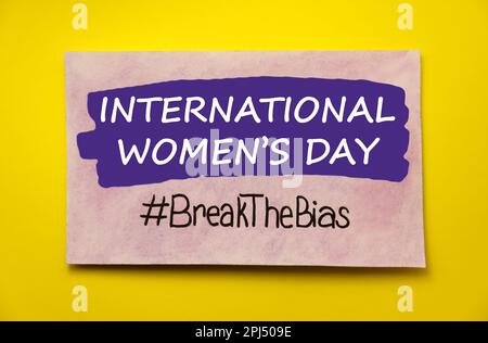 Scheda con testo Giornata Internazionale della Donna e hashtag BreakTheBias su sfondo giallo, vista dall'alto Foto Stock