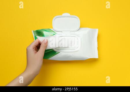 Donna che prende la salvietta bagnata dalla confezione su sfondo giallo, vista dall'alto Foto Stock