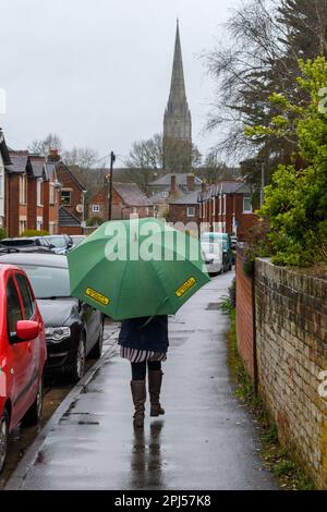 Salisbury, Wiltshire, Regno Unito, 31st marzo 2023: Donna con ombrello in tempo umido e ventoso l'ultimo giorno di marzo con la guglia della cattedrale di Salisbury sullo sfondo. Credit: Paul Biggins/Alamy Live News Foto Stock