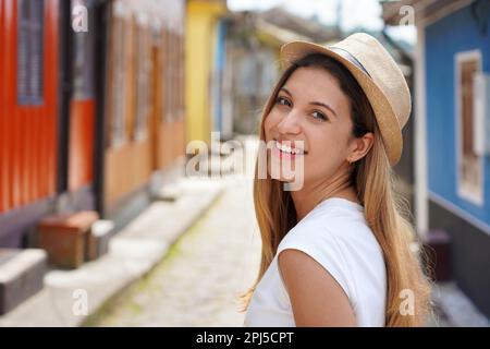 Primo piano di una giovane e felice donna turistica si gira e sorride alla fotocamera all'aperto Foto Stock