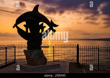 Preso come il sole sta scendendo dietro la statua dei due Delfini a Rethymnon, Creta, Grecia. Foto Stock