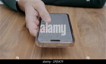 Smartphone man hand holding con app per il trading di titoli in valuta sullo schermo. Azioni di analisi finanziaria. Foto Stock