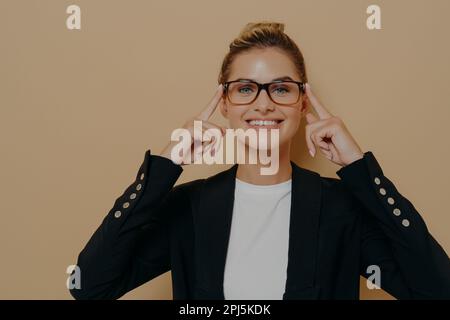 Studentessa bionda positiva che mette sugli occhiali e li tiene con le mani, giovane bella donna caucasica che posa e guarda attraverso lo spettacolo Foto Stock