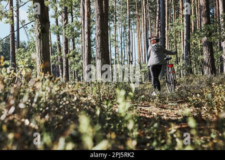 Donna attiva in bicicletta su strada forestale. Donna in bicicletta in fuoristrada percorso durante il giorno delle vacanze estive. Donna che indossa casco e guanti da bicicletta Foto Stock