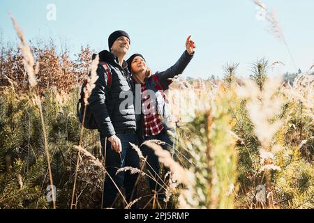 Coppia esplorando la natura durante il viaggio di vacanza. Escursionisti con zaini sulla strada per le montagne. Persone che camminano attraverso erba alta lungo il percorso in prato su sunn Foto Stock