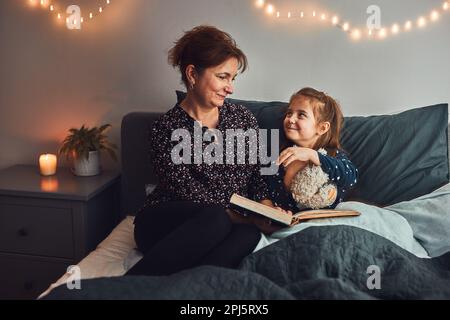 Mamma che legge libro sua figlia a letto prima di andare a dormire. Leggere storie prima di dormire. Storie di sonno per i bambini Foto Stock