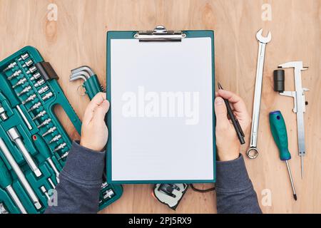 Uomo che lavora in officina tenendo gli appunti utilizzando molti strumenti. Chiave, chiave, pinza e cricchetto con molti accessori. Attrezzature. Utensile universale se Foto Stock