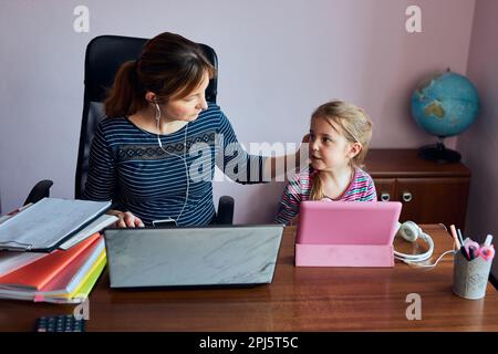Donna madre che lavora in remoto durante il webinar del corso online di videochat sul laptop da casa mentre sua figlia guarda un video Foto Stock