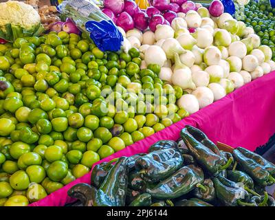 Varietà di verdure fresche in superficie con panno rosa in stallo nel mercato messicano, tomatillo, verde poblano cile, cavolfiore, cipolla bianca e viola Foto Stock